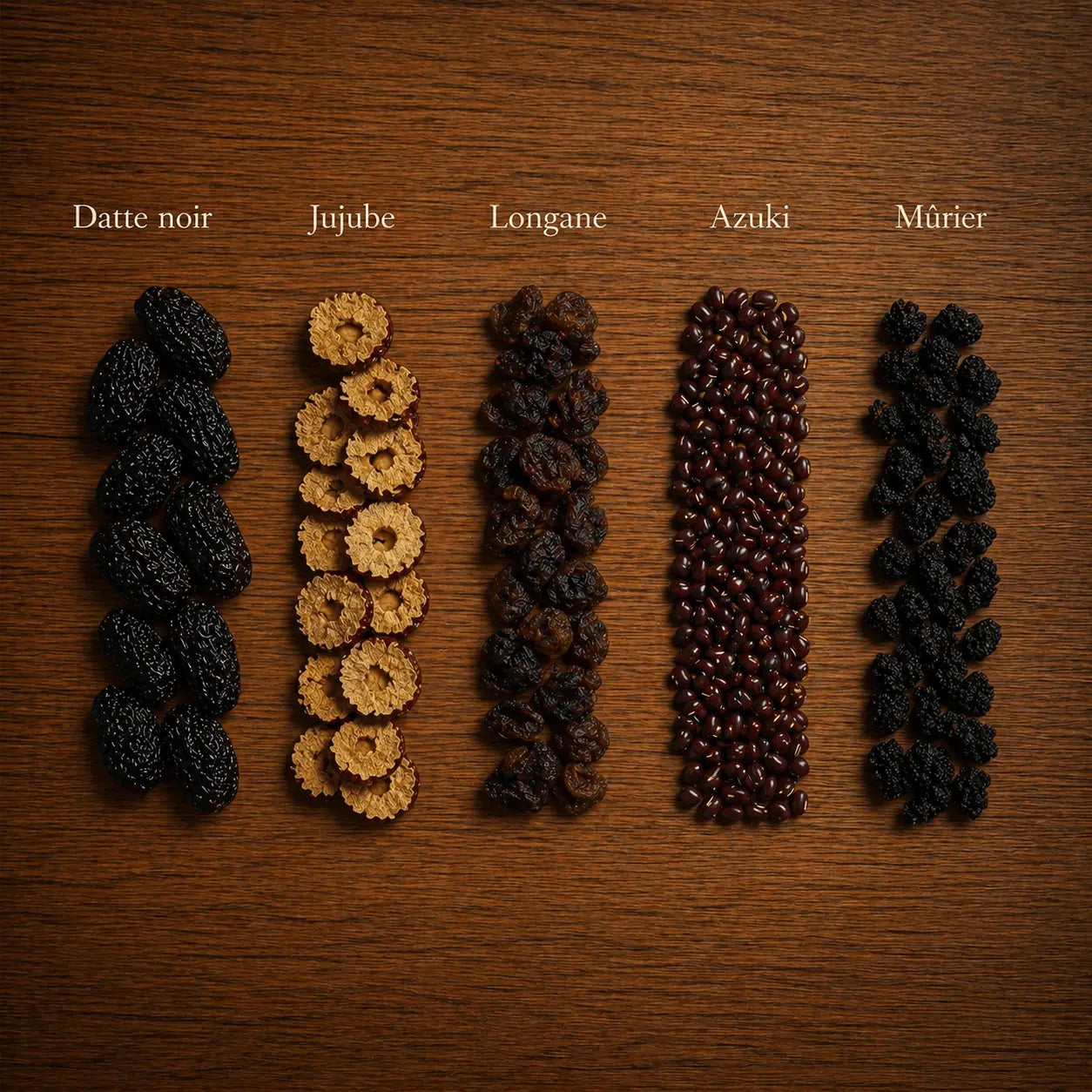 Cinq ingrédients de l'infusion énergie N°14 THÉCHA : datte noire, jujube, longane, azuki et mûrier, disposés sur un fond en bois naturel